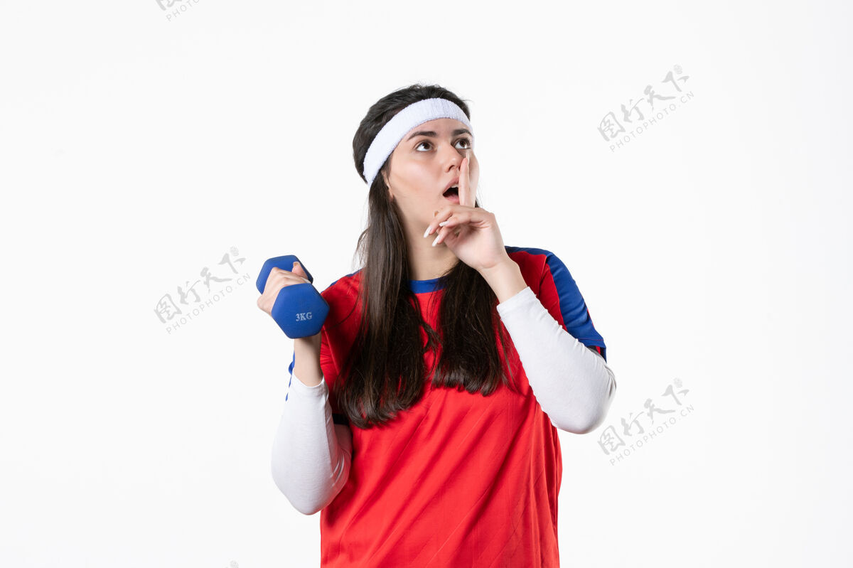 微笑正面图穿着运动服的年轻女性在白墙上用哑铃锻炼球员哑铃年轻女性