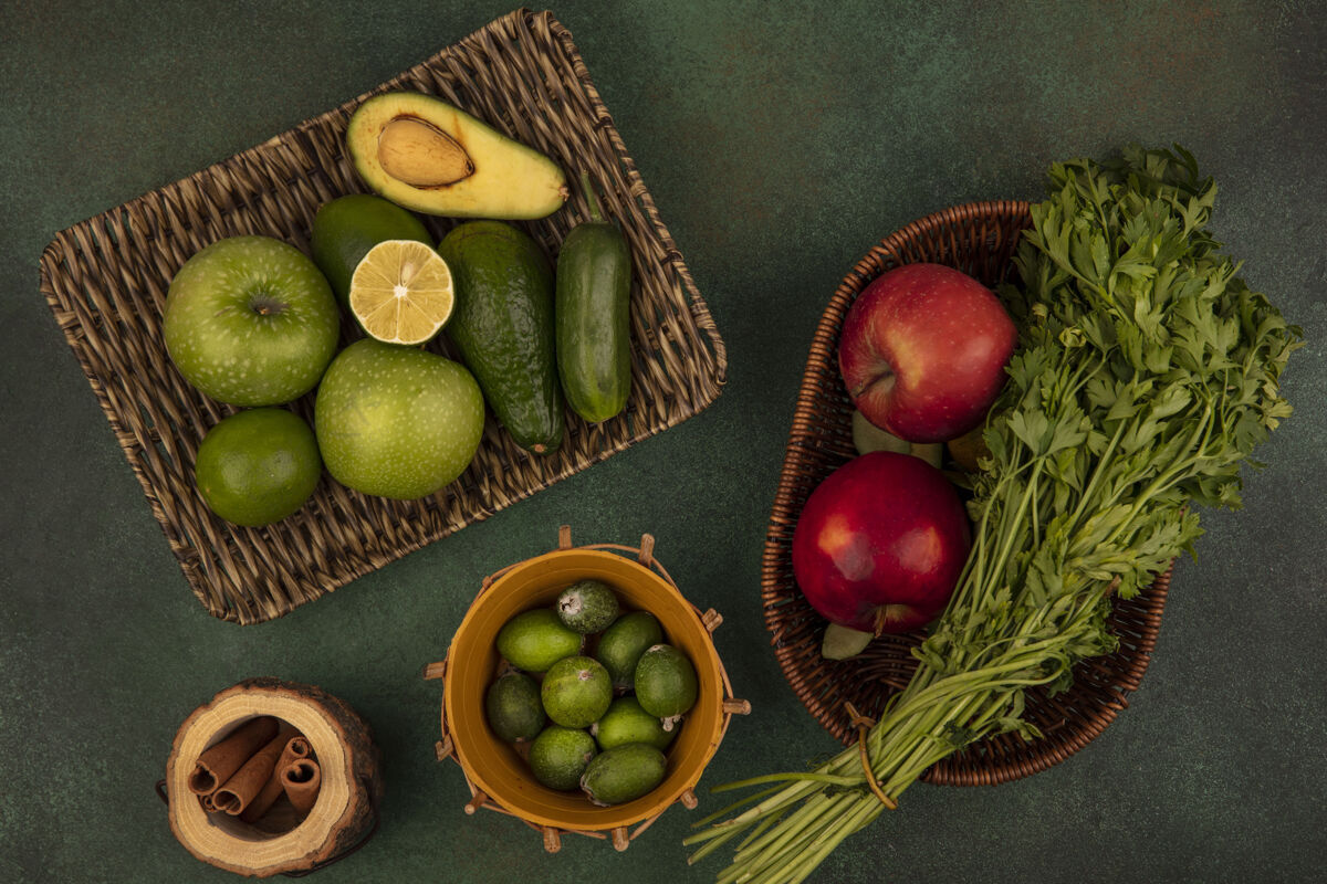 新鲜新鲜食物的俯视图 如绿色的苹果 鳄梨 柳条托盘上的黄瓜 桶上的飞珠 桶上的红苹果和欧芹 在绿色的墙上鳄梨饮食食物