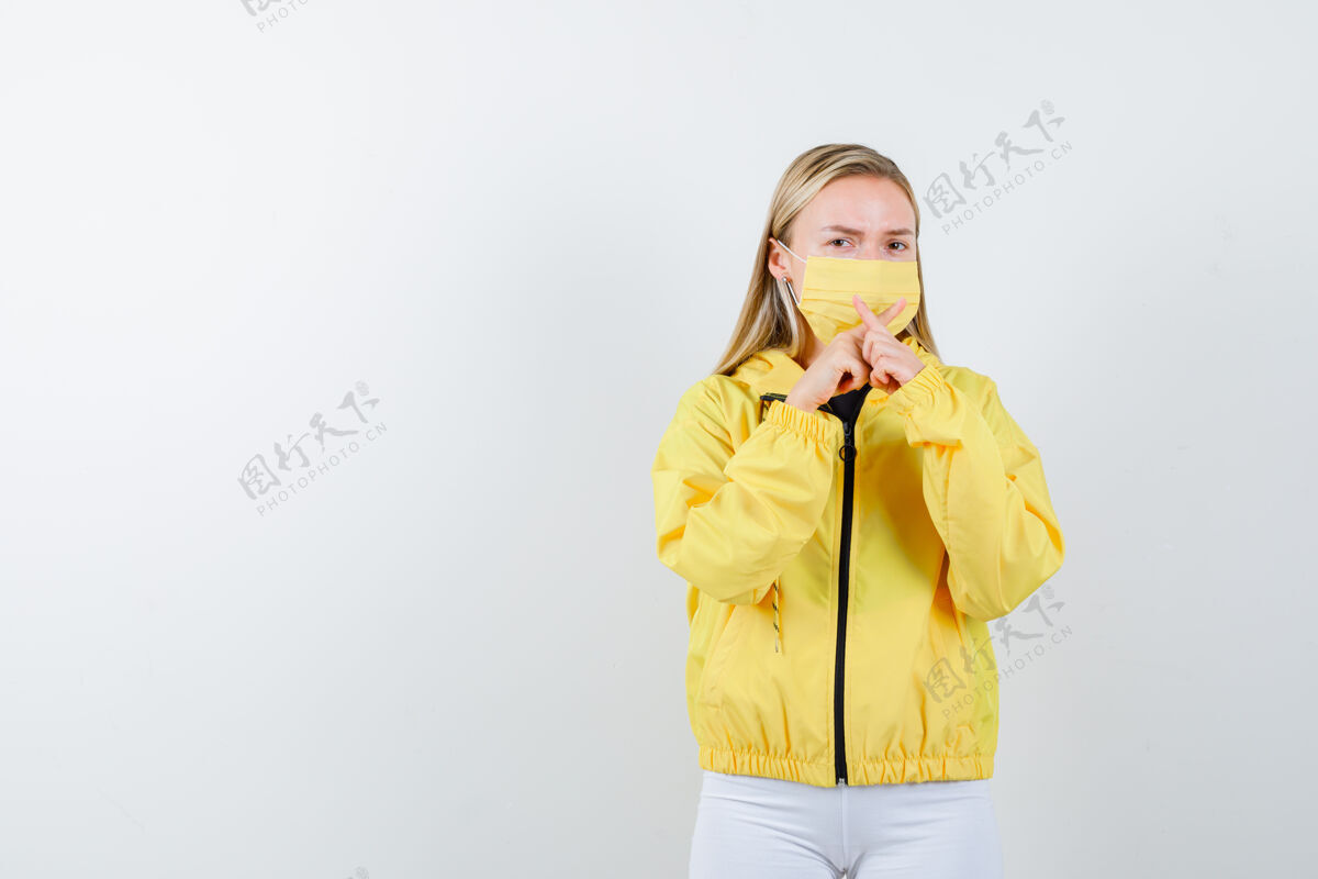 夹克穿着夹克 裤子 面具的年轻女士用交叉的手指做了一个“x”形的沉默手势 仔细地看着前方的景色手指沉默皮肤