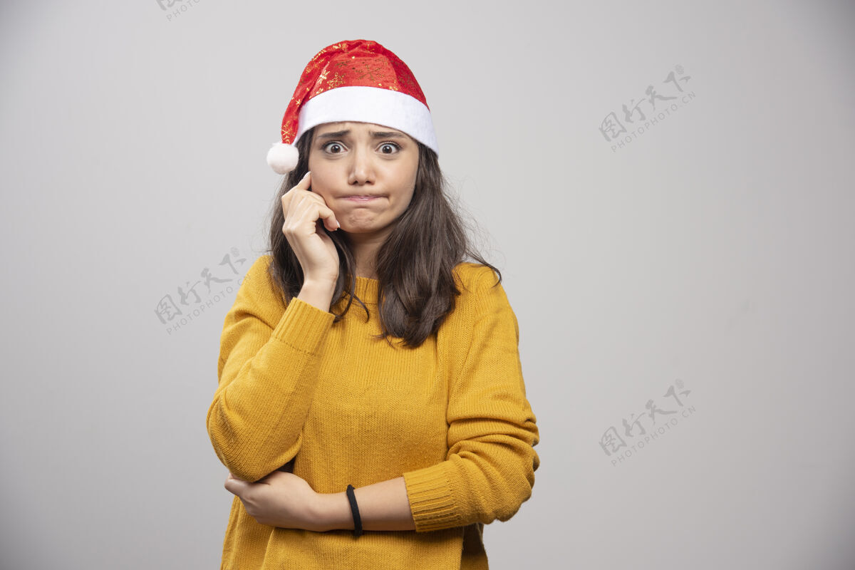 圣诞节戴着圣诞老人红帽子的年轻女子在白墙上摆姿势礼品盒人姿势