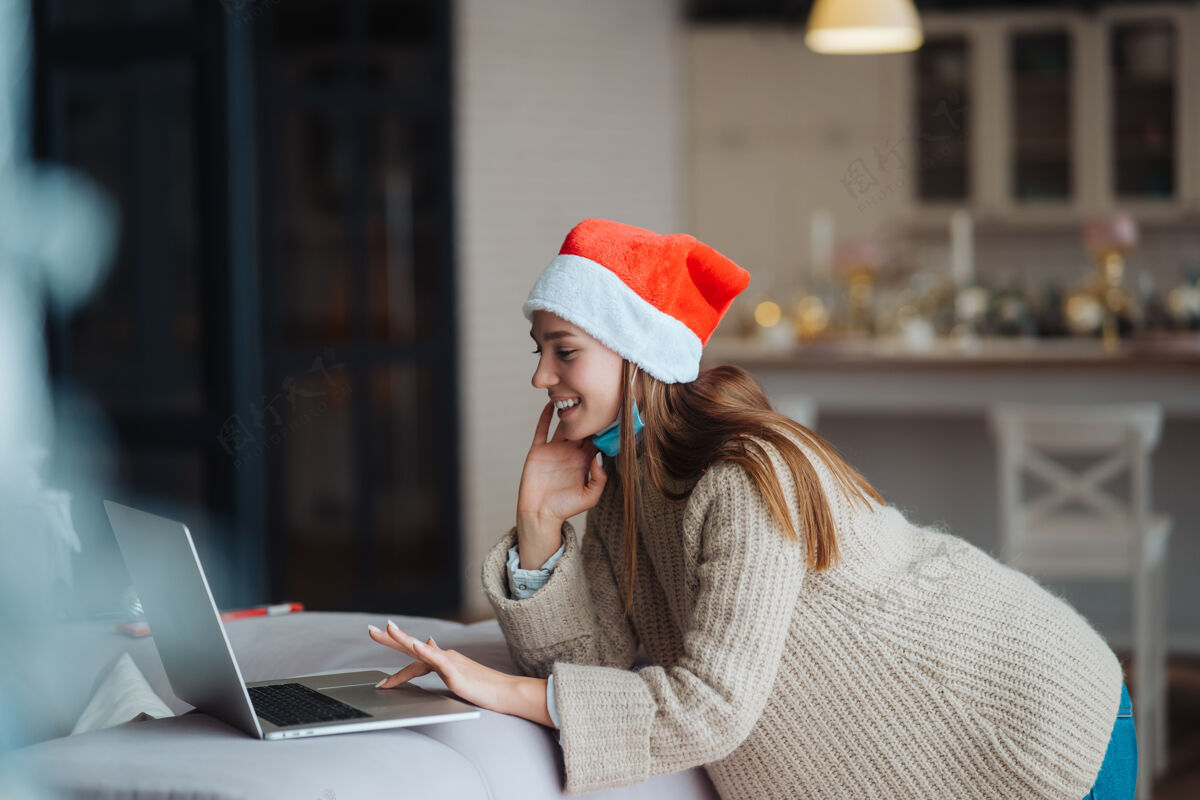 节日在家里庆祝圣诞节的时候 一个戴着圣诞老人的女人微笑着用笔记本电脑和网友聊天惊人圣诞节人