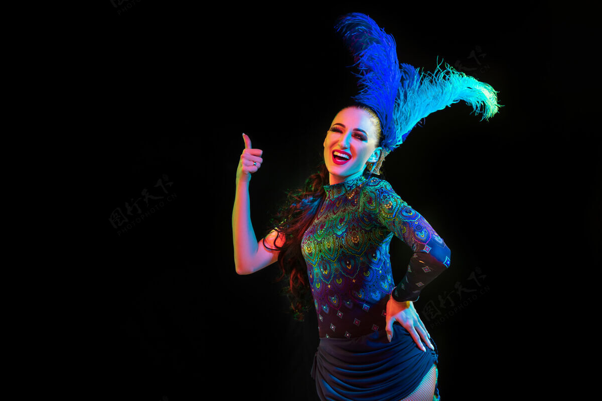 魅力美丽的年轻女子在嘉年华 时尚的化装服装与羽毛的黑色背景在霓虹灯下人类节日传统