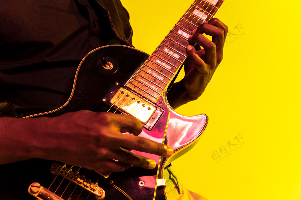 成人年轻的非洲裔美国音乐家在霓虹灯下像摇滚明星一样在黄色背景下弹吉他娱乐天才音乐会
