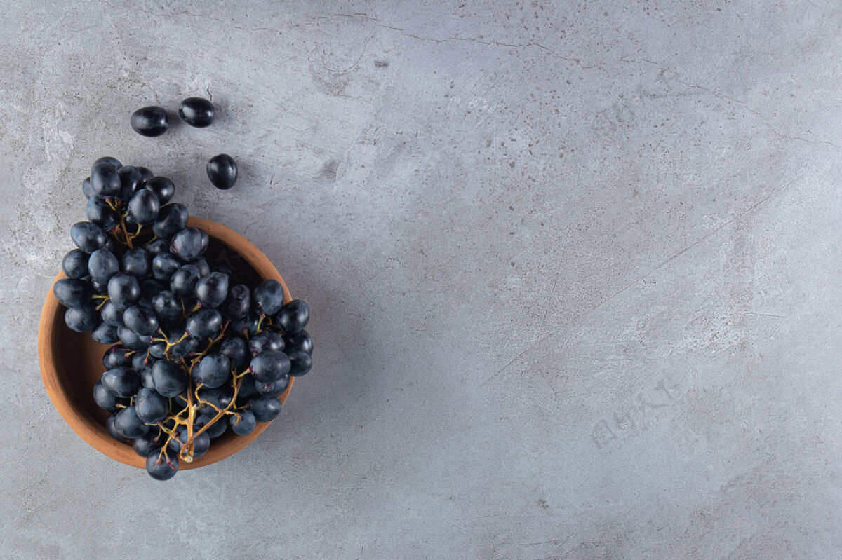 食物石头桌上放着一块木板 上面放着新鲜的黑葡萄和一杯葡萄酒平坦美味水果