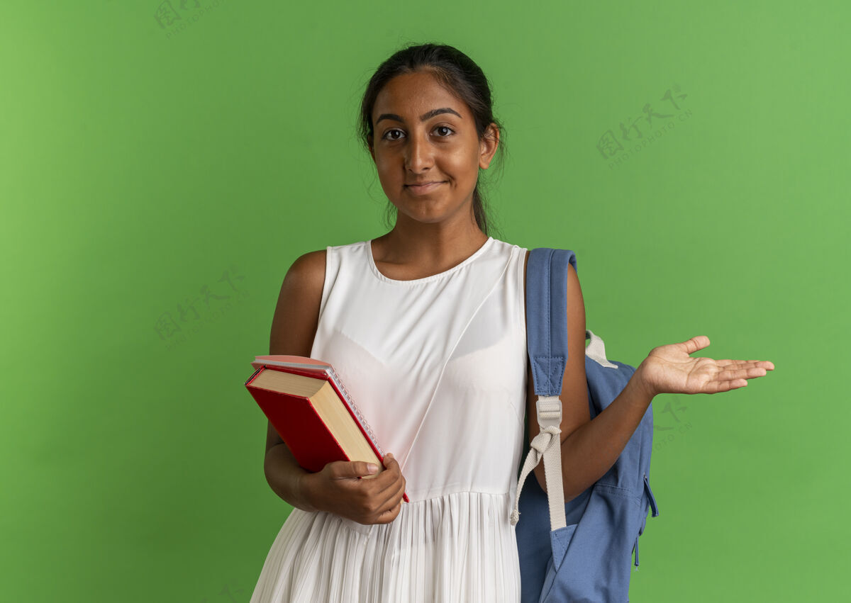 绿色高兴的小女生背着书包拿着笔记本 摊开手孤立在绿色上包手摊开