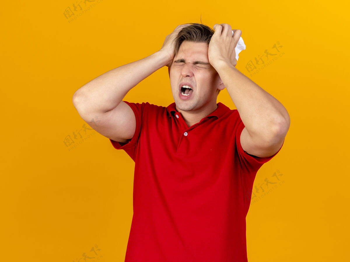 表情疼痛的年轻英俊的金发病患拿着餐巾双手放在头上头痛闭着眼睛隔离在橙色的墙上人人脸