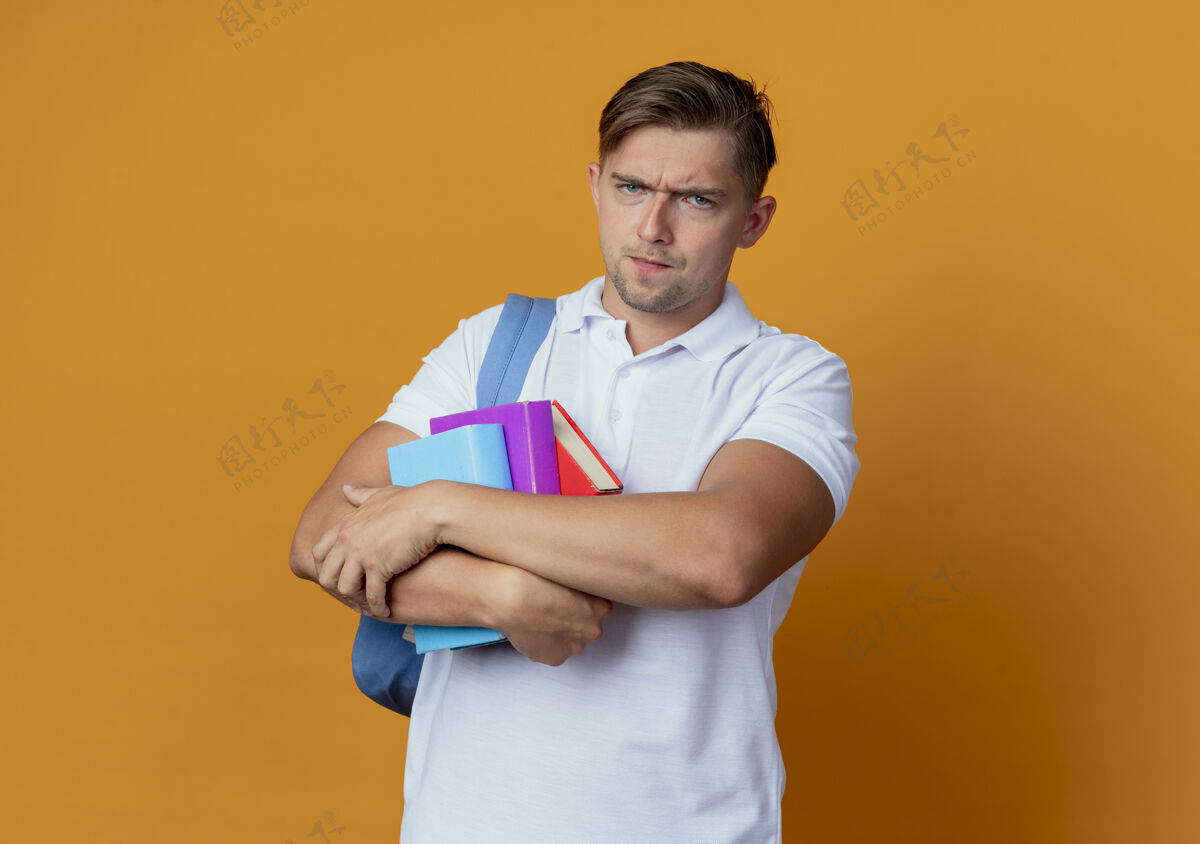 穿严格的年轻帅气男学生背着书包拿着书孤立在橘子上严格背抱
