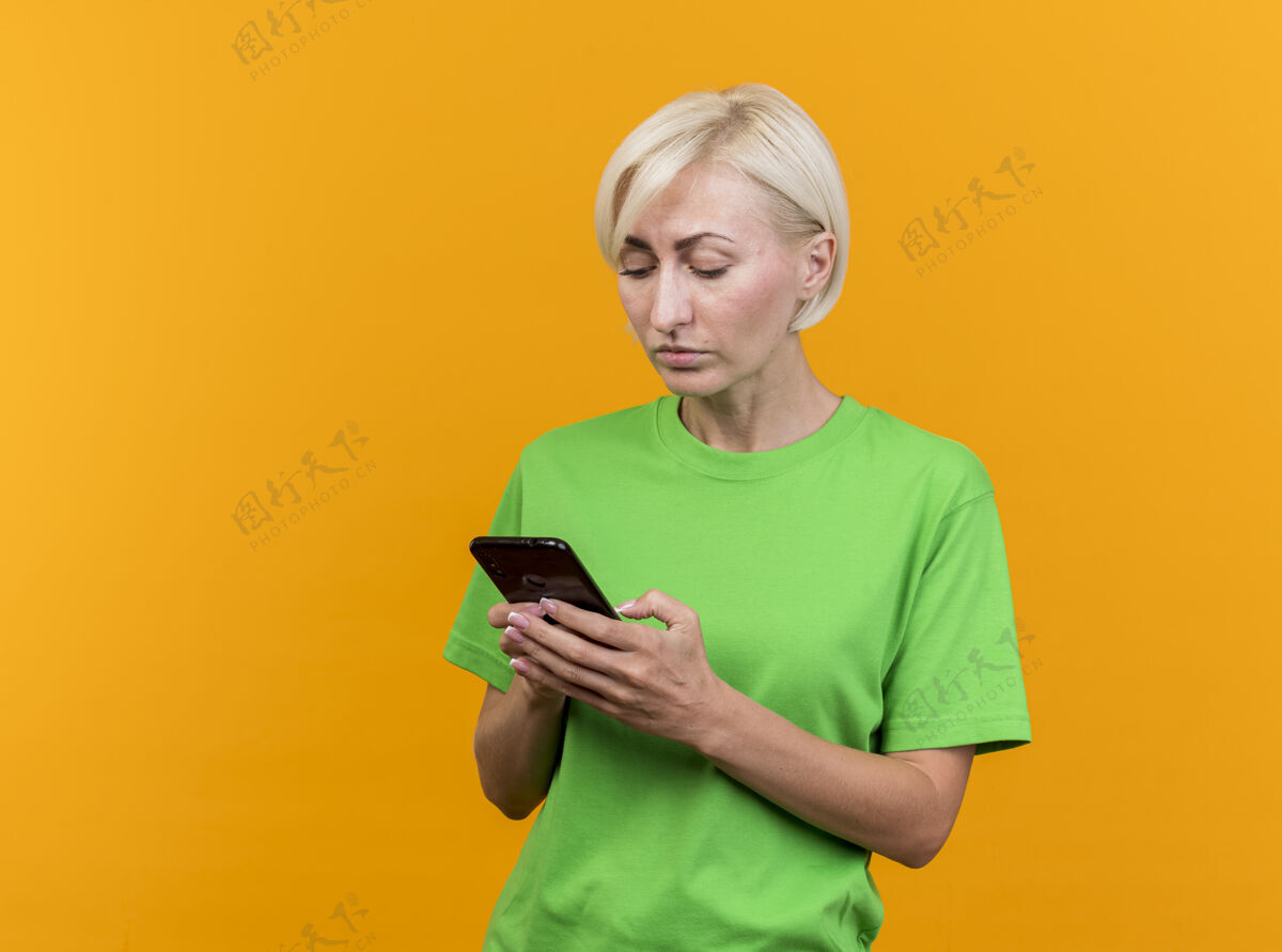 人专注的中年金发女人用手机隔离在黄色的墙上衣服人市民