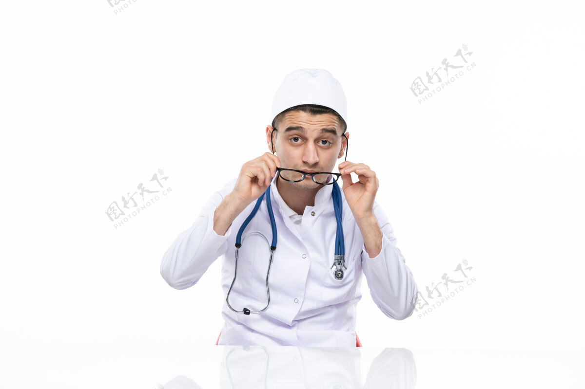 套装正面图：年轻的医生穿着医疗服坐在桌子后面坐着前面男人