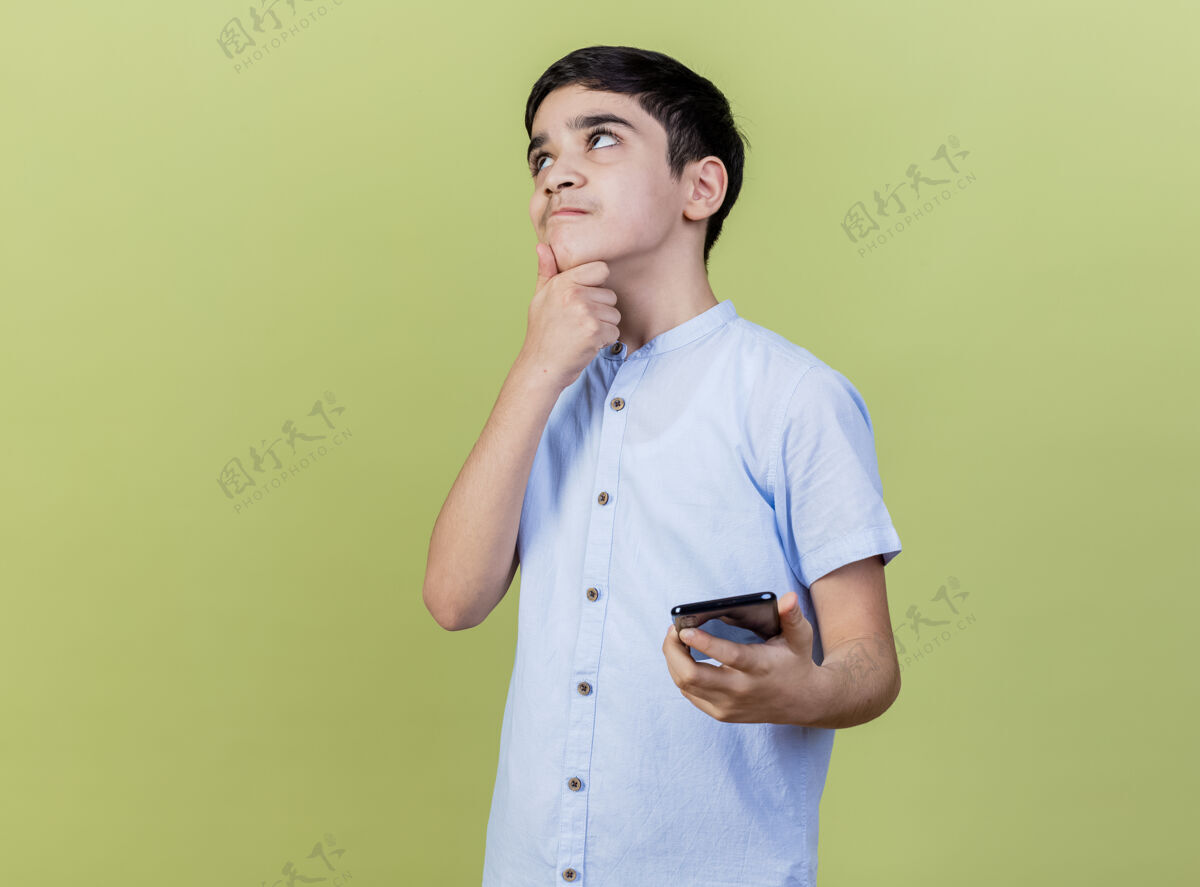 衣服体贴的小男孩拿着手机摸着下巴 孤零零地看着橄榄绿的墙上脸表情手机