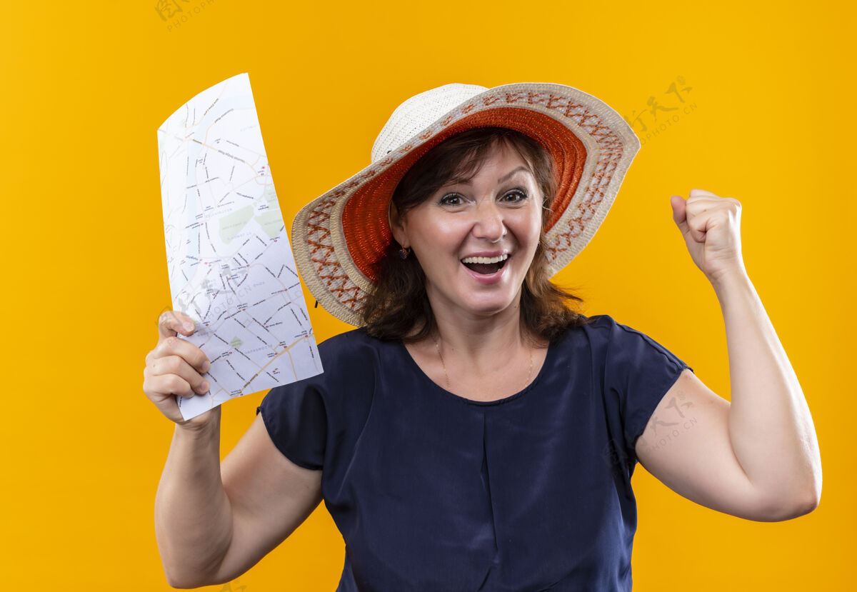 表演快乐的中年旅行家妇女 戴着帽子 拿着地图 在孤零零的黄墙上做着“是”的手势帽子地图中年