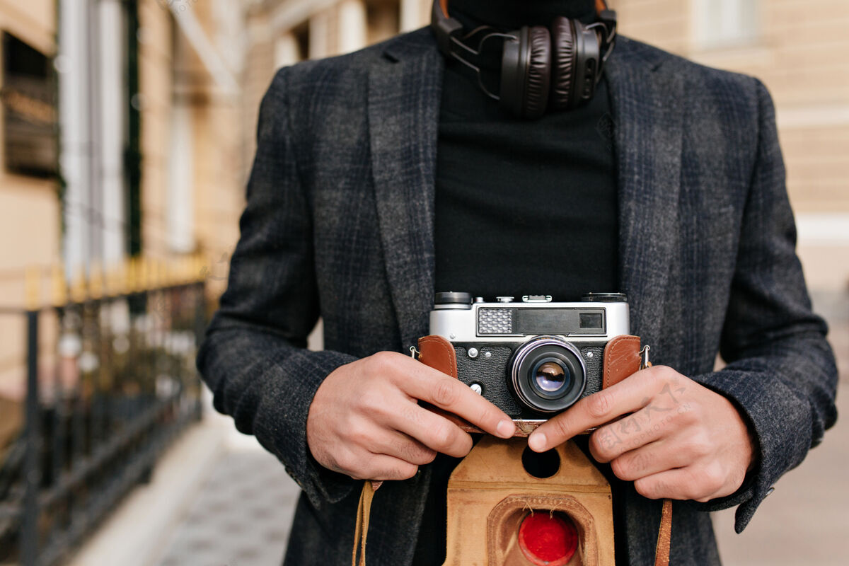 混血儿一个穿着黑色衬衫和灰色夹克的男人在街上的特写照片摄影师拿着相机 浅棕色皮肤的照片配饰成人黑发