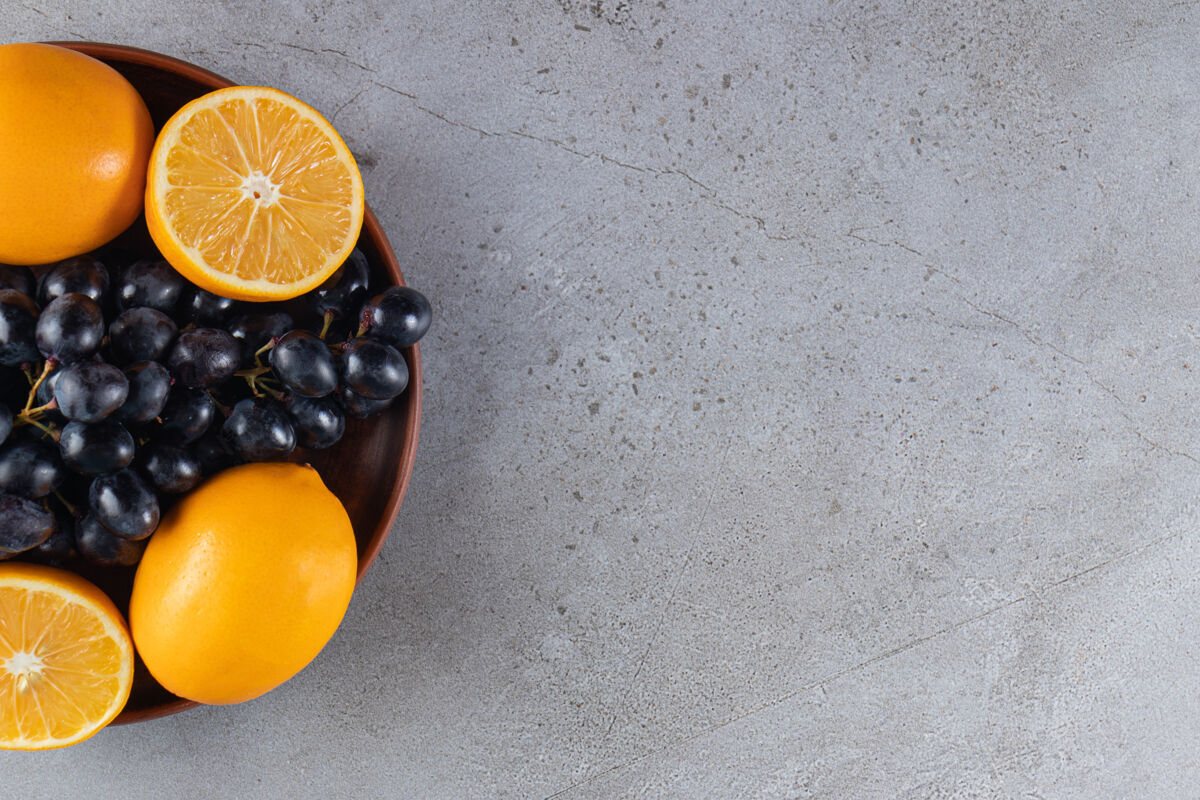 有机石头桌上放着一大盘新鲜的黑葡萄和橙子葡萄多汁美味