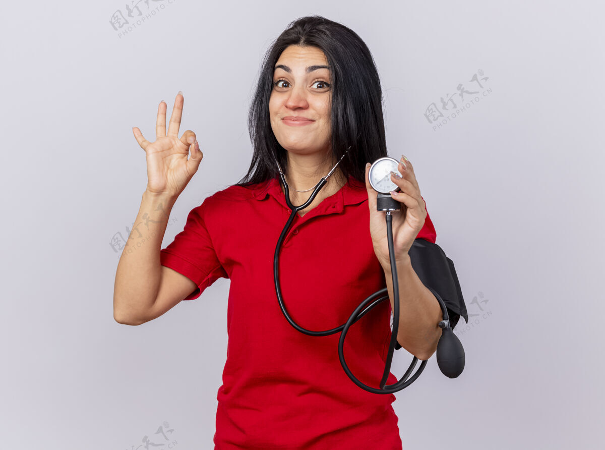 女人戴着听诊器的年轻病患高兴地看着前面 用血压计测量她的血压 在白色的墙上隔离了一个正常的标志人人请