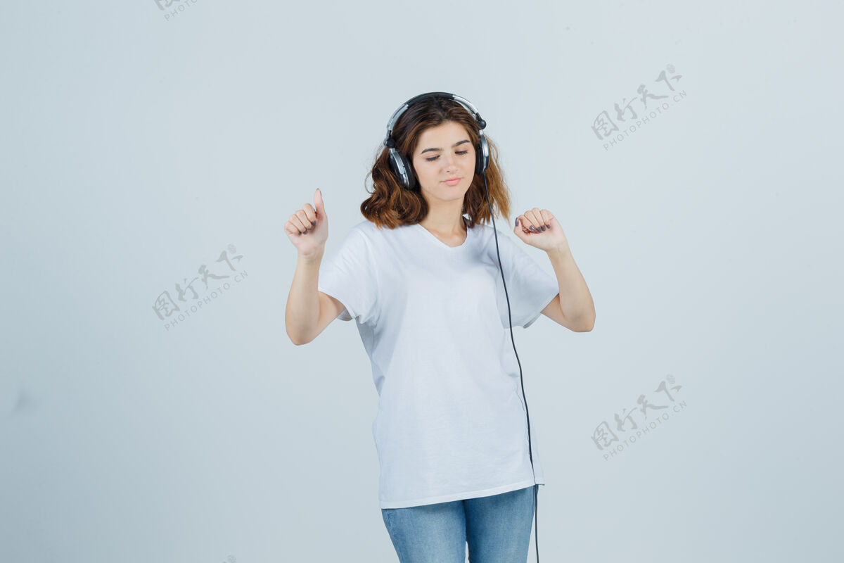 头发穿着白色t恤 牛仔裤 戴着耳机欣赏音乐的年轻女性的肖像 看上去很快乐卷发牛仔裤微笑