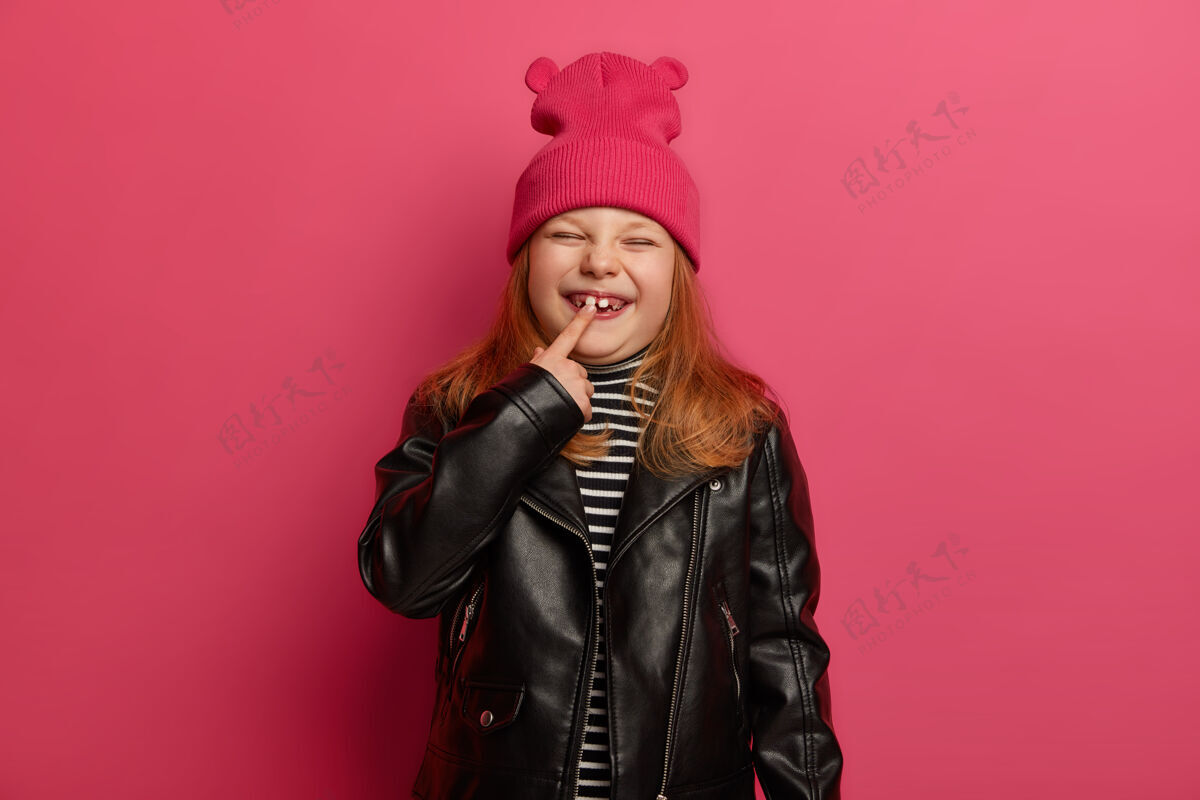 小快乐的小姜女 穿着时尚的衣服 指着她的新牙 有着难忘的童年 愉快地眯着眼睛 对着明亮的粉色墙壁摆姿势孩子们的成长理念指标有趣风格