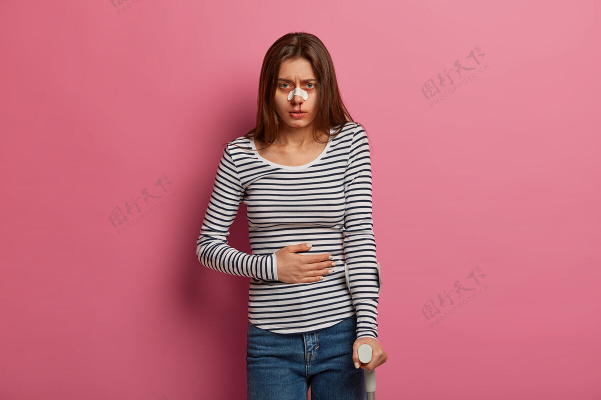 哭泣年轻人因疼痛而皱眉 感到胃痛 身体有损伤 接受康复计划 鼻子有血 隔离在粉红色的墙壁上健康问题概念室内痛苦残疾