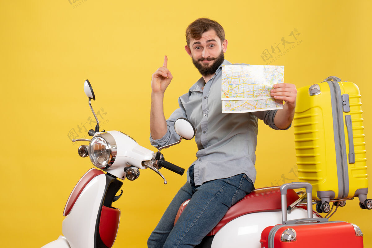 摩托车旅游概念与年轻的情感胡须男子坐在摩托车上 并指向前方举行地图指向它的黄色持有摩托车旅游