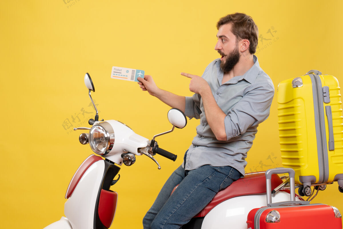 车辆旅游概念的正面图 年轻惊讶的胡须男子坐在摩托车上指着黄色的车票人摩托车旅游