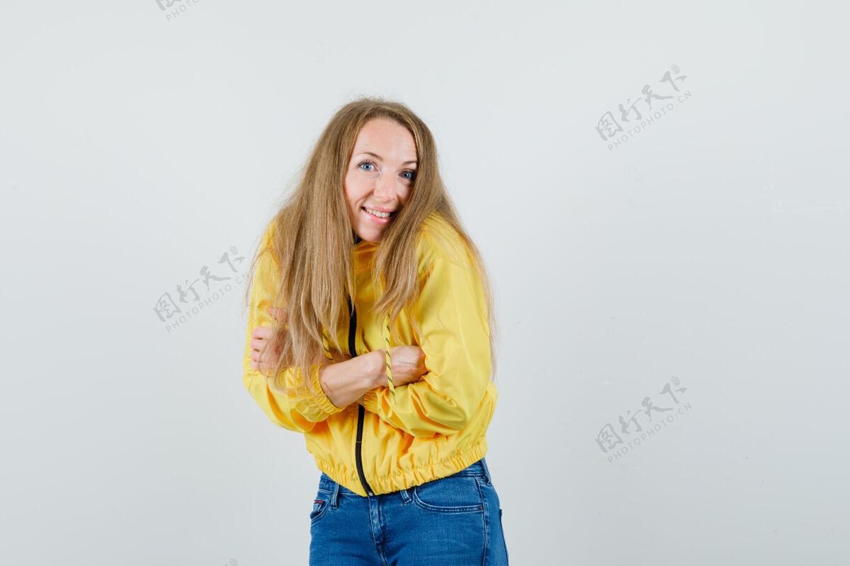 漂亮身穿黄色棒球服和蓝色牛仔裤的年轻女子交叉双臂站在镜头前 看上去很乐观 正面照时尚年轻前面
