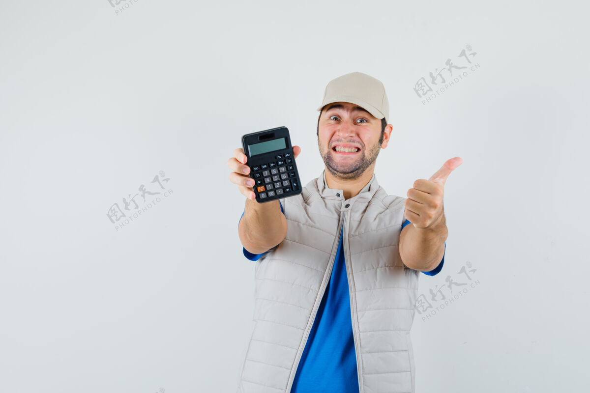 拇指年轻人展示着计算器 大拇指朝上 穿着t恤衫 夹克衫 看上去很高兴 正前方的景色男人聪明朋友
