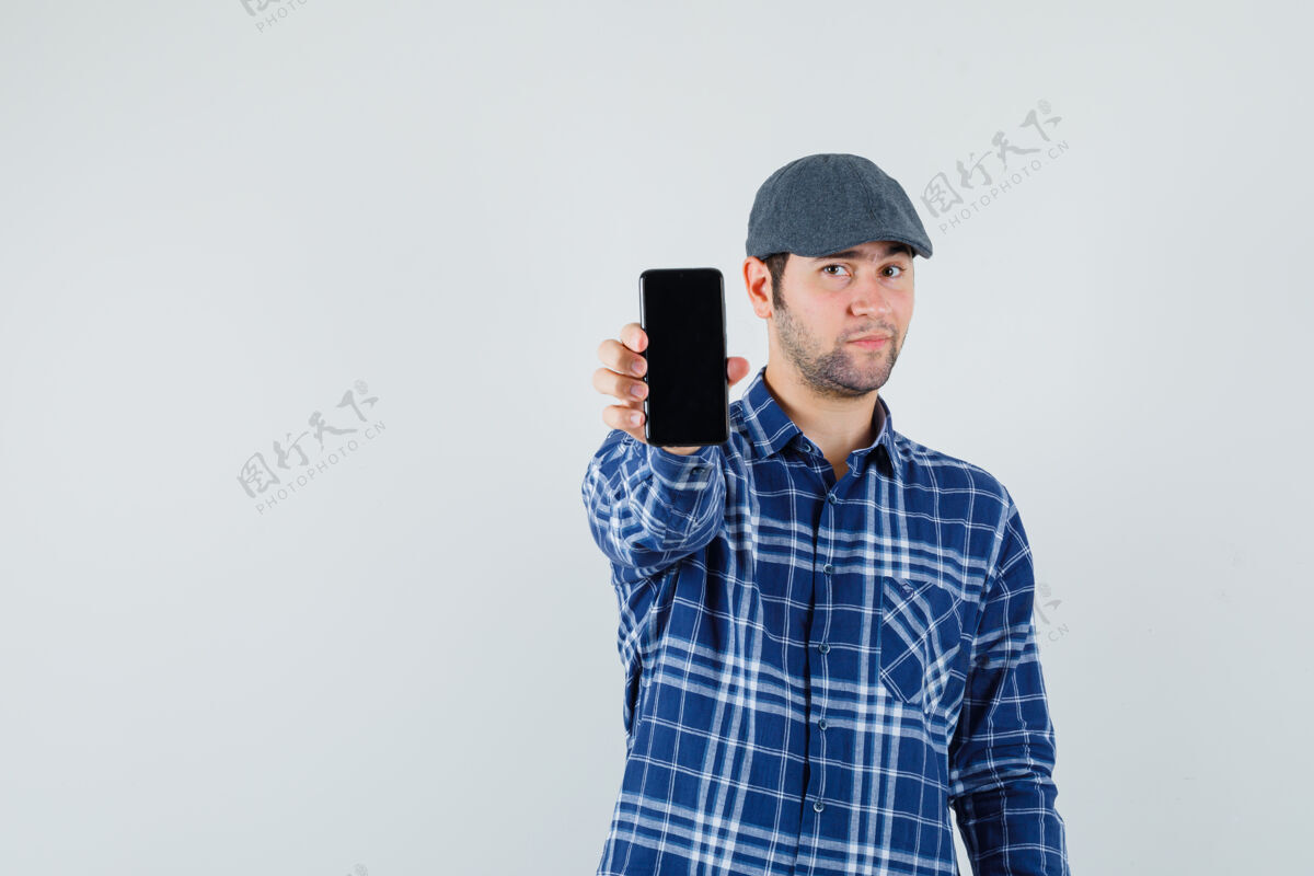 男士穿着衬衫 戴着帽子的年轻人展示着手机 看上去很自信 正对着前方休闲聪明手机