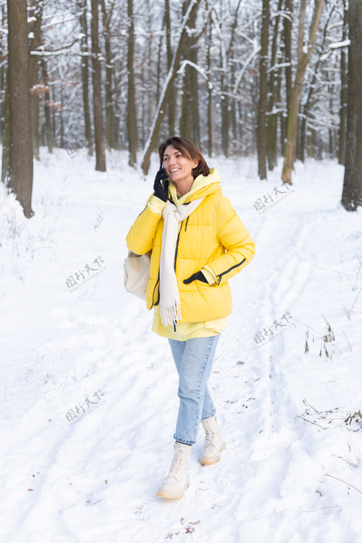 年轻心情愉快的快乐女人漫步在雪域的冬日森林里 愉快地聊着电话 享受着公园里的户外时光节日帽子女性
