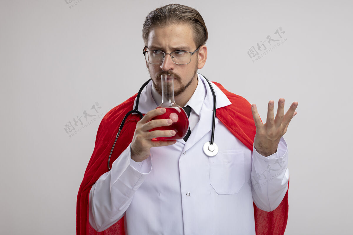 瓶子年轻的超级英雄 穿着医用长袍 戴着听诊器和眼镜 拿着一个装满红色液体的化学玻璃瓶 在白色的背景上隔离持有思考长袍