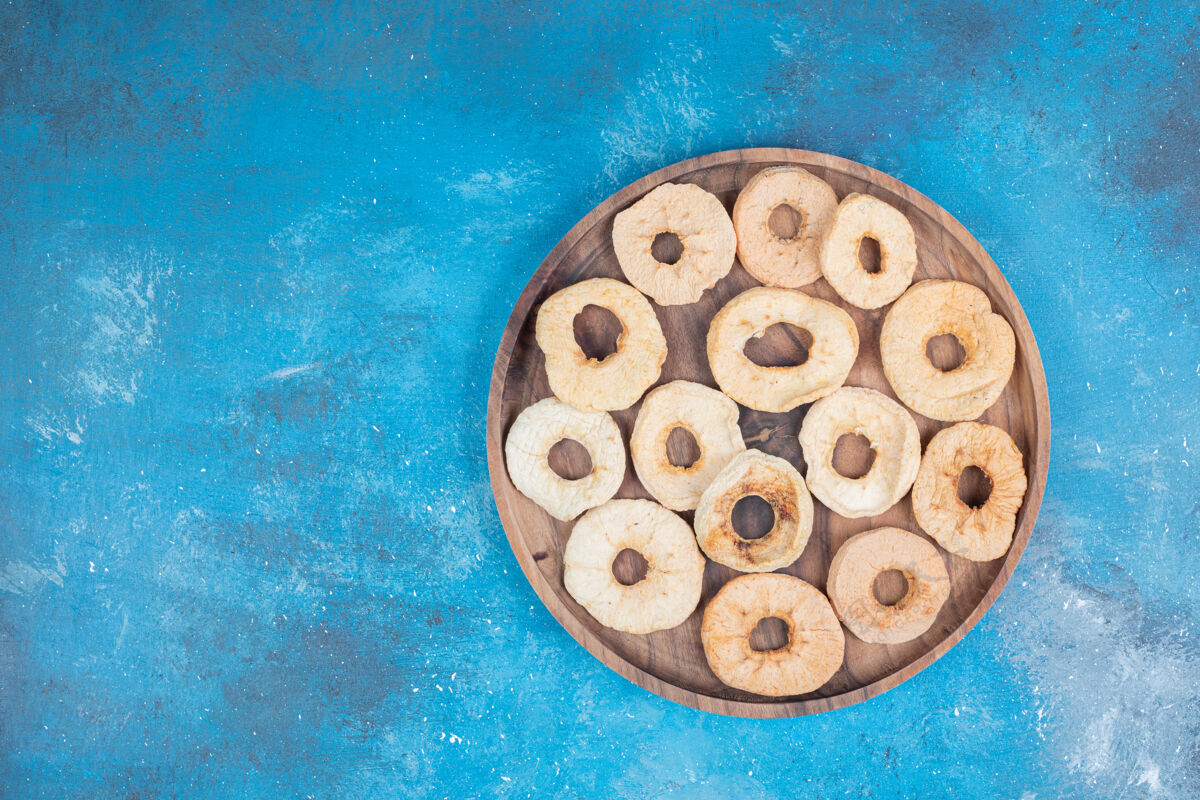 切片干苹果片放在蓝色表面的木板上蓝色薯片零食