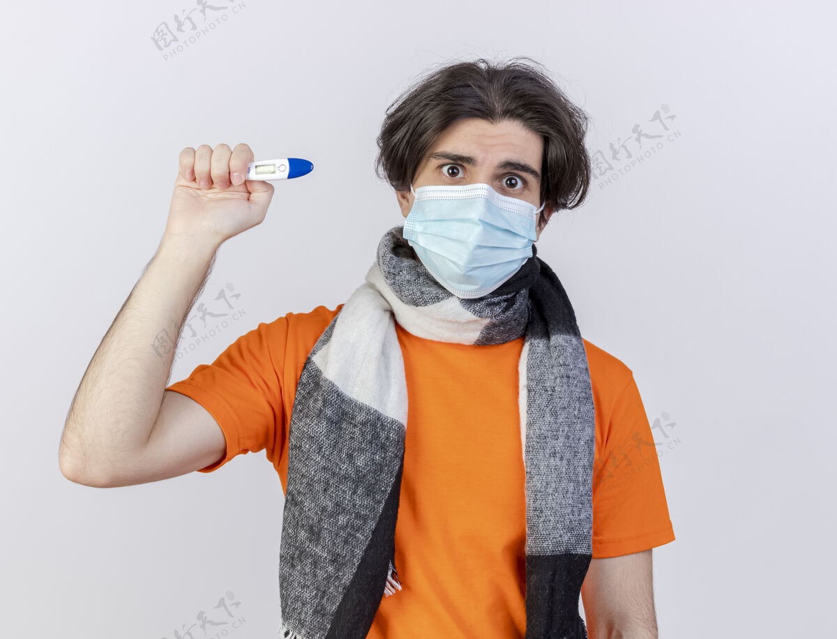 体温计惊讶的年轻人戴着围巾和医用面罩拿着温度计隔离在白色背景上年轻医疗疾病