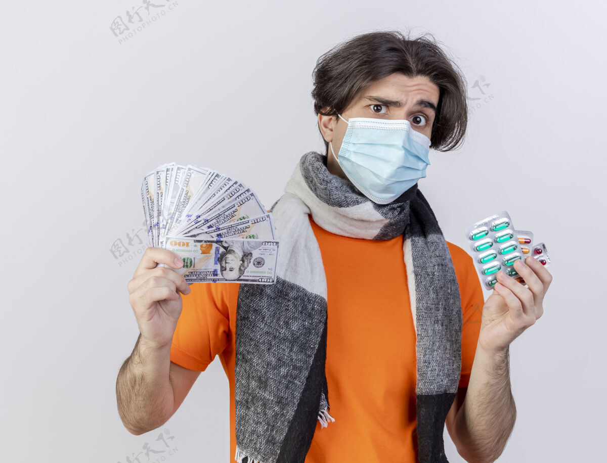 迷茫困惑的年轻病人戴着围巾和医用面罩拿着现金和隔离在白色背景上的药片围巾医疗疾病