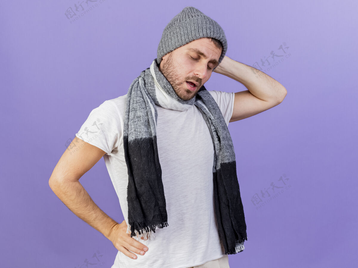 手闭着眼睛 戴着带围巾的冬帽 手放在头上 臀部隔离在紫色背景上的年轻病人头封闭帽子