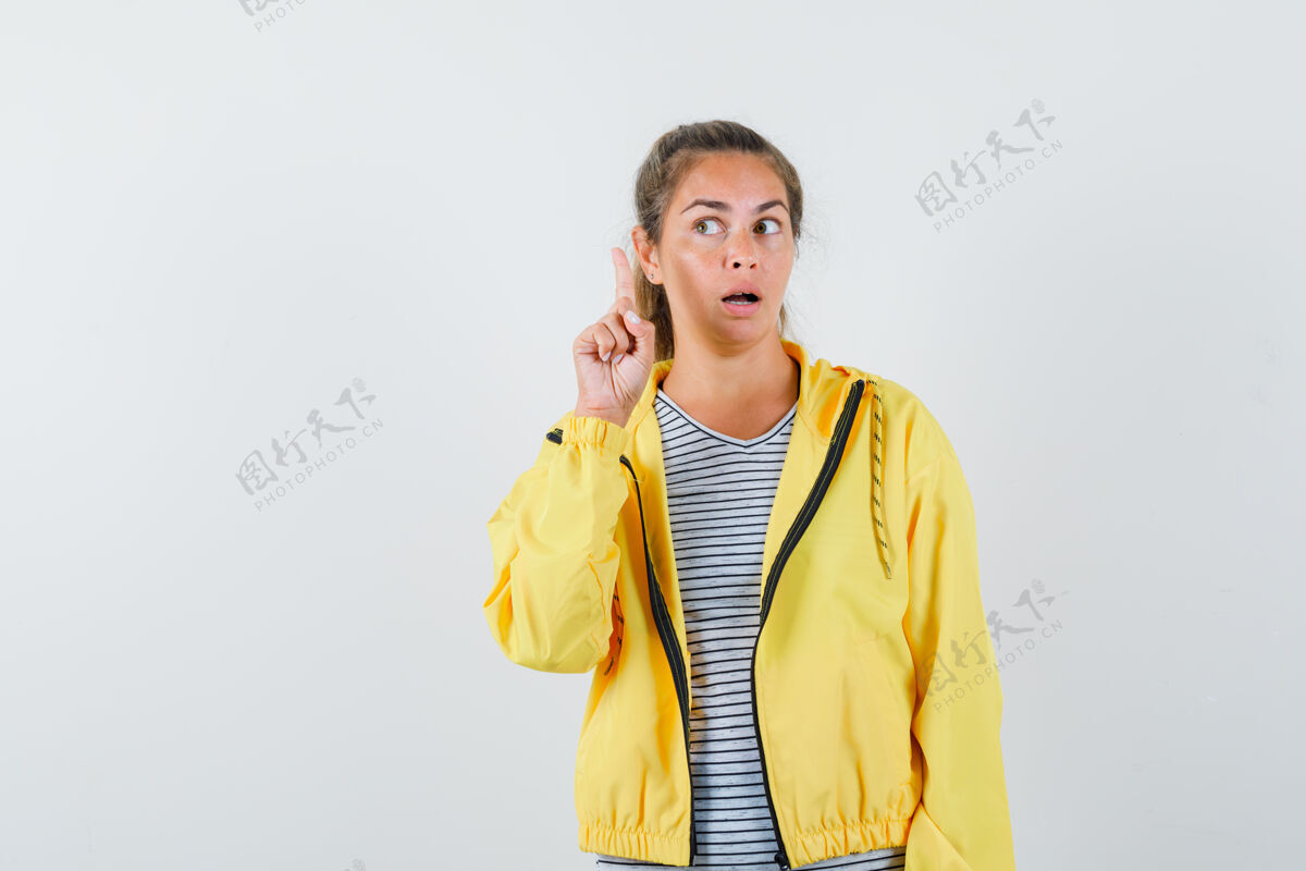 严肃金发女人举着食指做着尤里卡手势 穿着黄色棒球服和条纹衬衫看着它 看起来很严肃肖像女人头发