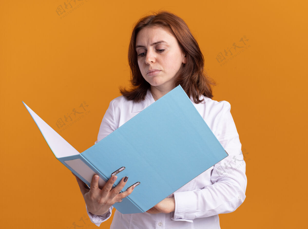 开身穿白衬衫的年轻女子拿着打开的文件夹 严肃地看着它站在橙色的墙上女人夹脸