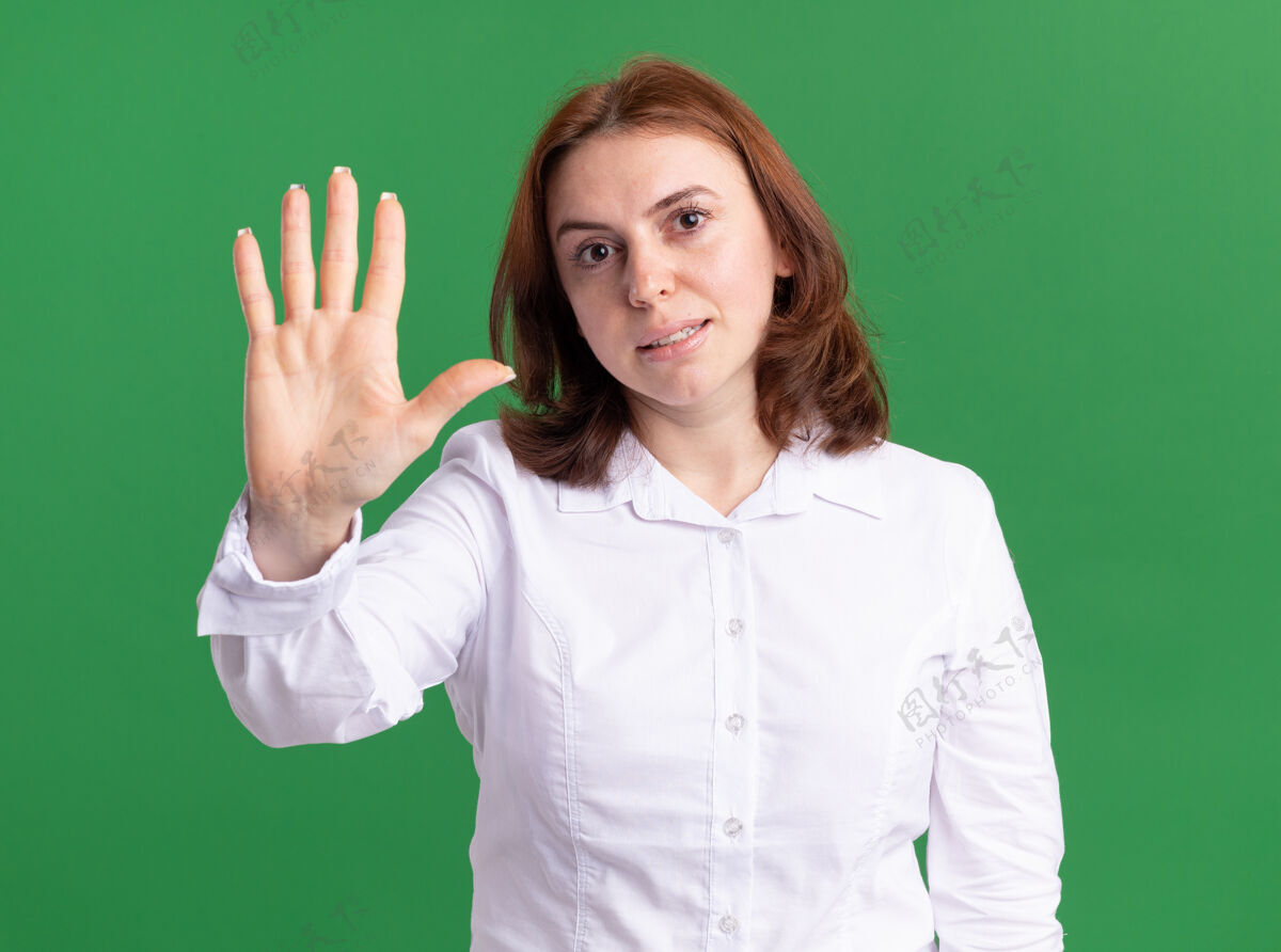 衬衫身穿白衬衫的年轻女子看着前面的展台 用手指着第五个微笑着站在绿色的墙上指指点点年轻五