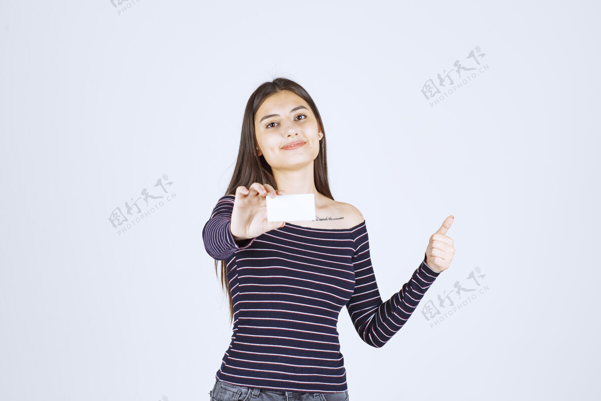 员工穿条纹衬衫的女孩拿着名片 举着拇指朝上的牌子成功年轻雇员