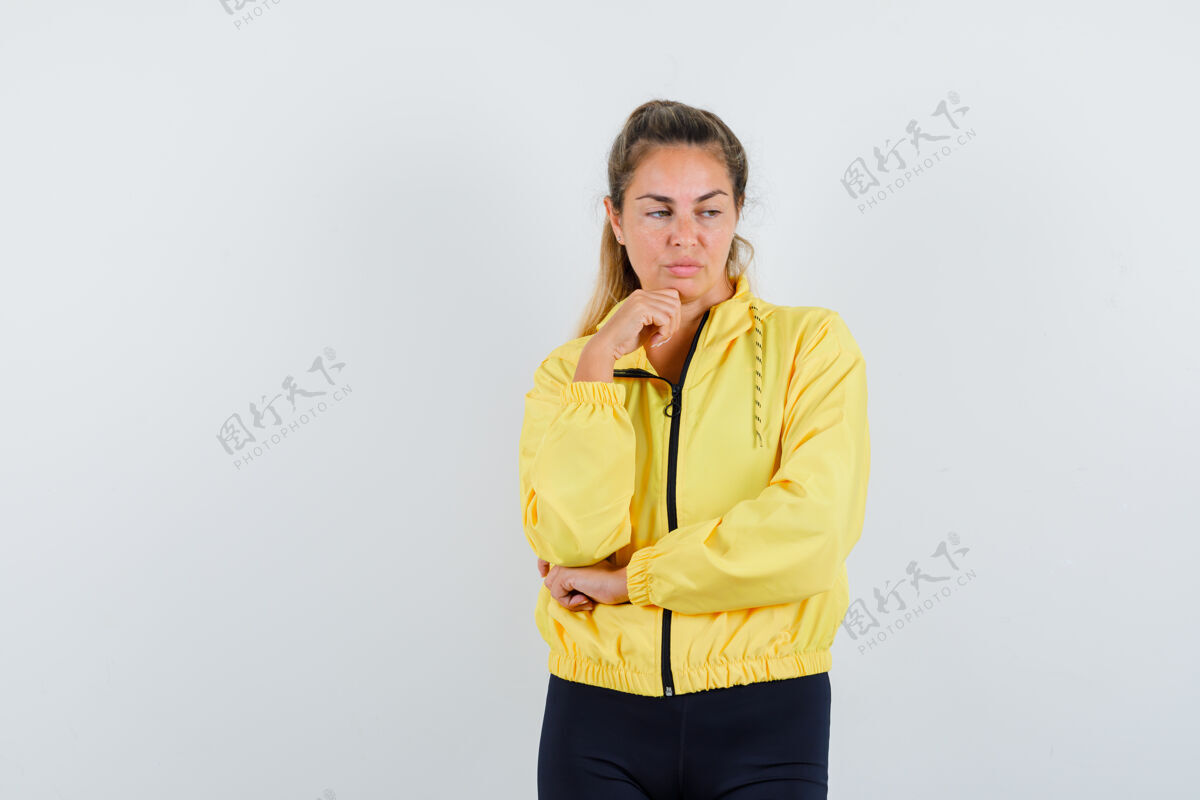 思考穿着黄色棒球服和黑色裤子的金发女人站在思考的姿势 手托下巴 看起来沉思瘦头发脸