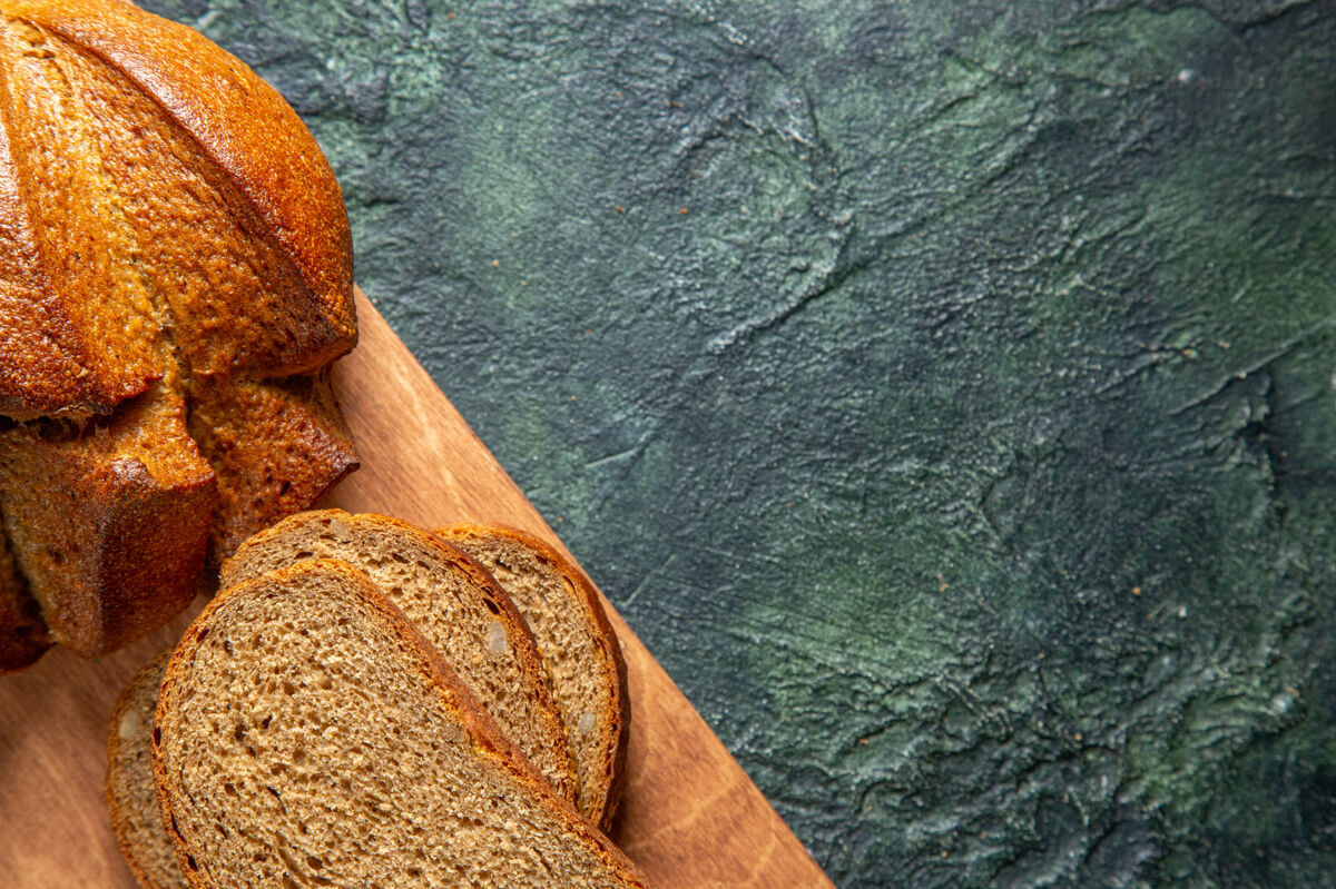 早餐在深色背景的棕色木砧板上拍摄半张完整的黑面包新鲜木板一半