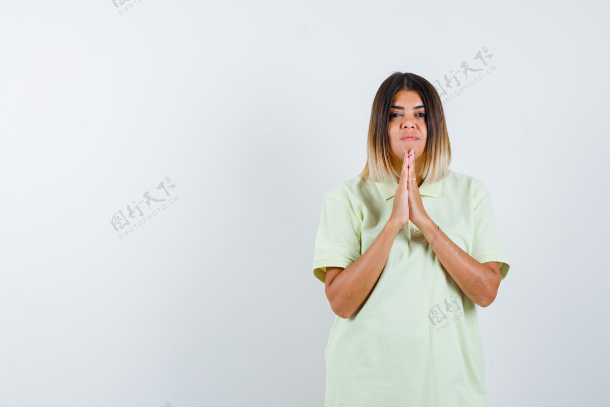 前面年轻的女孩紧握双手祈祷的立场 在t恤衫 并期待着认真的 前视图销售皮肤扣