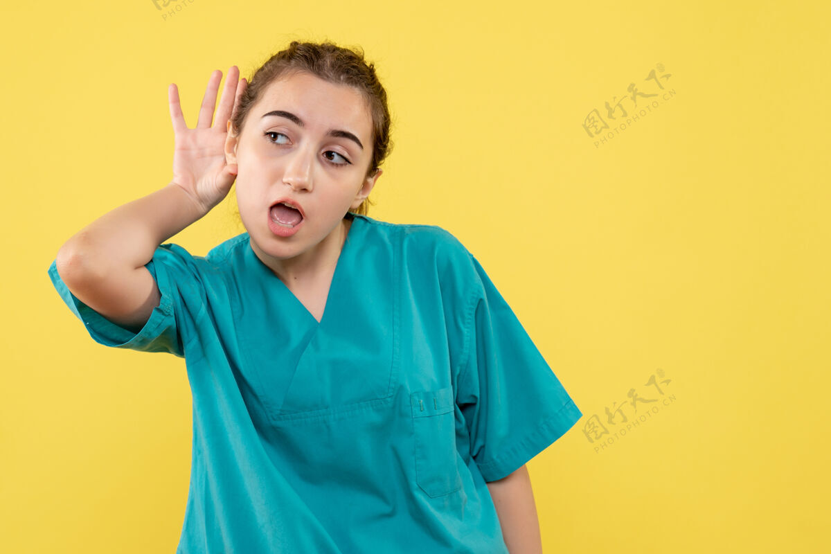 肖像身着医疗服的女医生在黄色墙壁上聆听的正视图套装快乐女医生