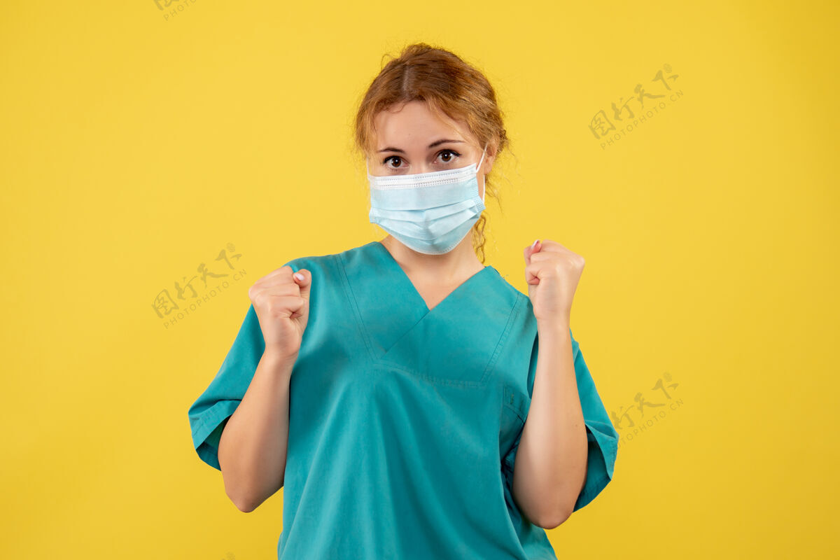 加强黄色墙壁上穿着医疗服 戴着口罩的女医生的正视图人面罩成人