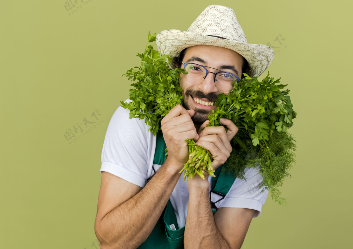绿色戴着园艺帽 戴着眼镜 面带微笑的男园丁手里拿着茴香和香菜帽子复制穿