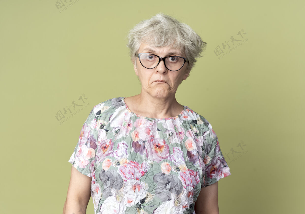 绿色惊讶的戴眼镜的老妇人在橄榄绿的墙上孤零零地向前看橄榄色惊喜老年人