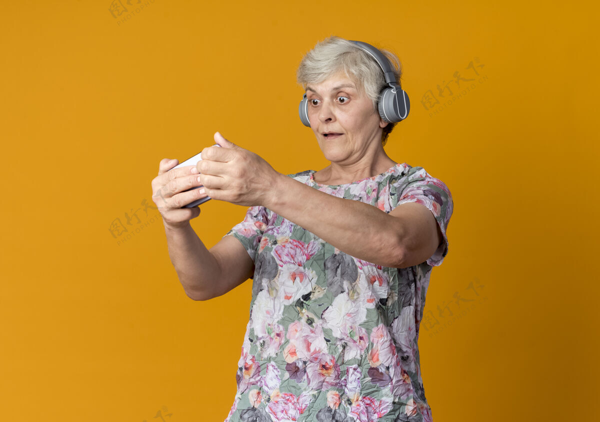 拿着惊讶的老妇人拿着耳机 看着电话孤零零地挂在橘黄色的墙上惊喜老人耳机