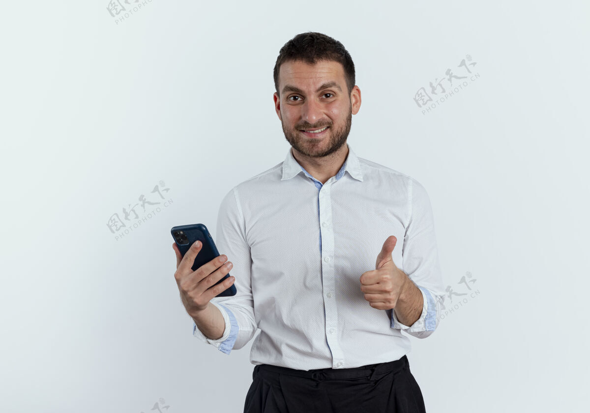 男人笑容可掬的帅哥拿着手机 竖起大拇指孤零零地站在白墙上拇指商人向上