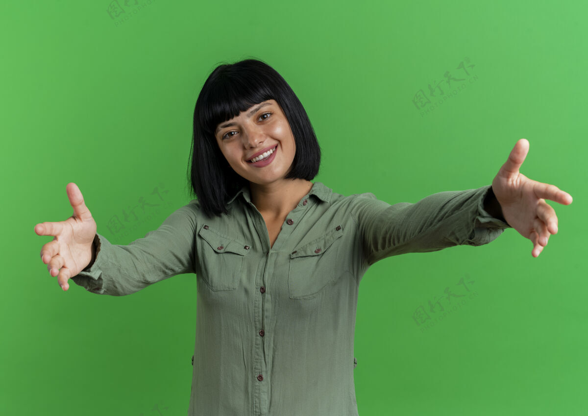 黑发微笑的年轻黑发白种女人伸出双手孤立在绿色背景与复制空间伸展背景年轻