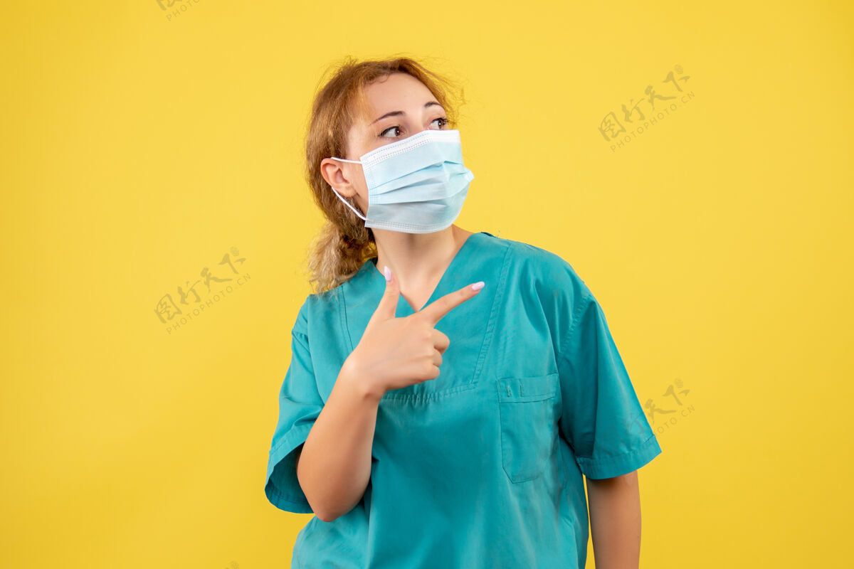 面具黄墙上穿着医疗服 戴着无菌口罩的女医生的正面图健康大流行人