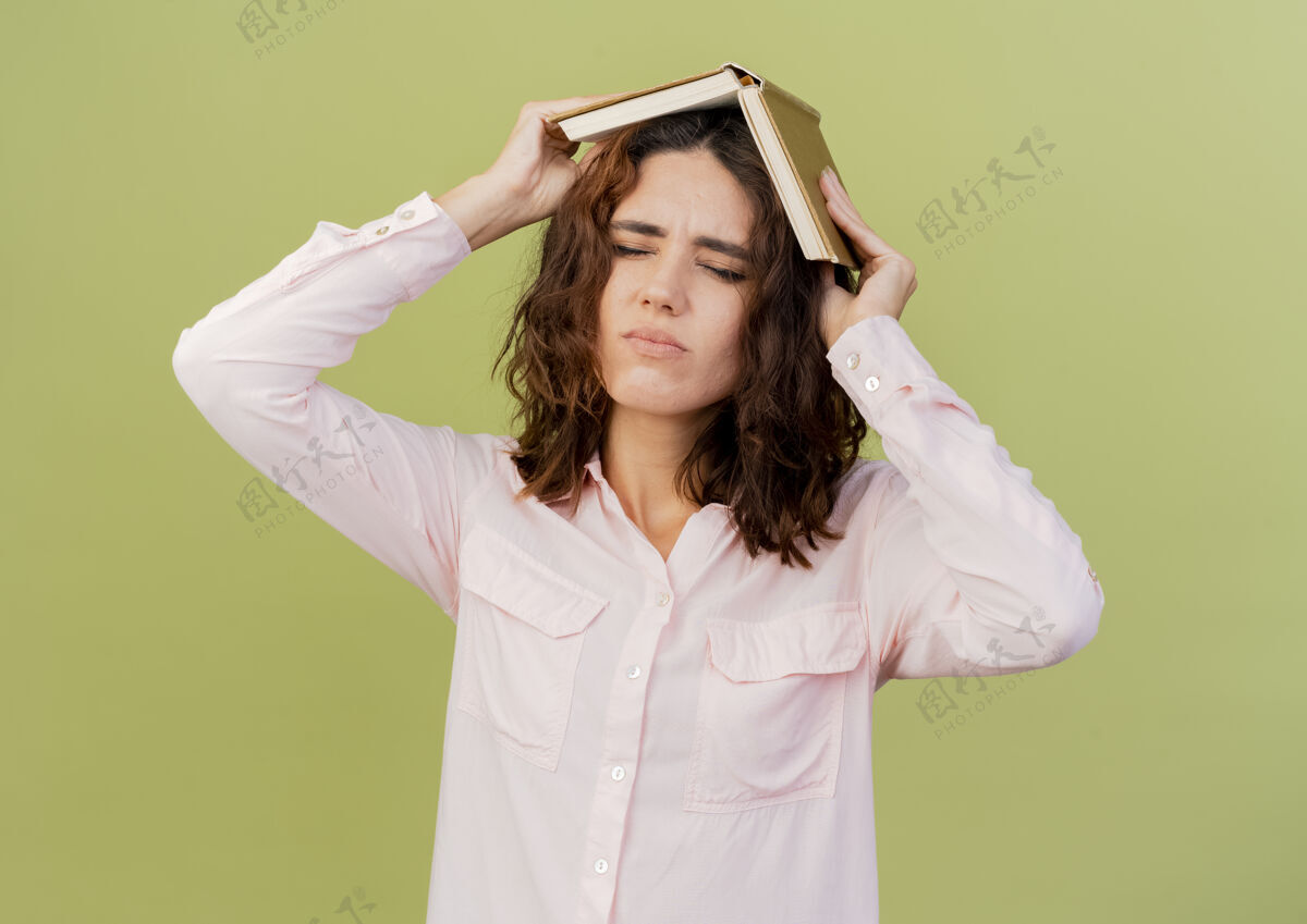 女人恼怒的年轻白种女人把书举过头顶 孤立地放在绿色背景上 留着复印空间背景头烦恼
