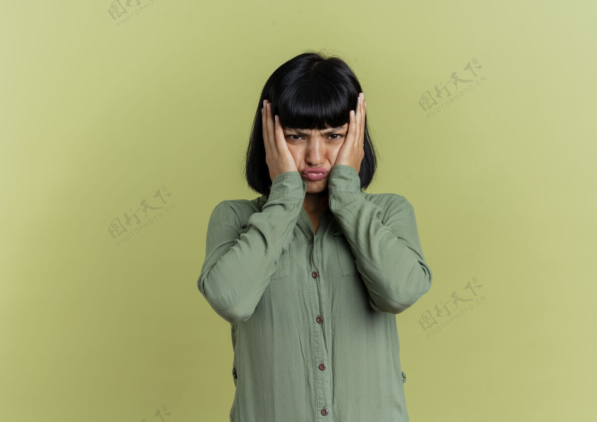 女人年轻的黑发白种女人把手放在橄榄绿背景上的脸上 并留有复印空间橄榄脸不愉快