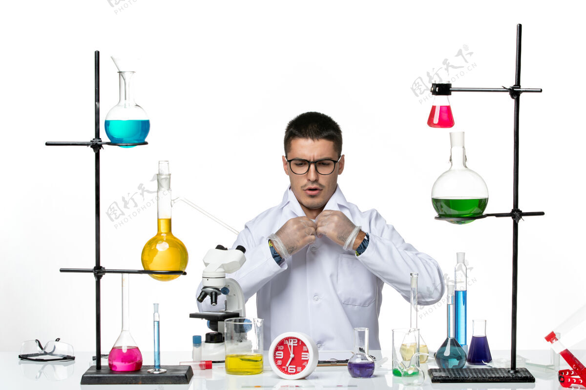 实验正面图穿着白色医疗服的男性化学家坐在白色办公桌上准备工作病毒科学冠状病毒-大流行实验室容器大流行玻璃